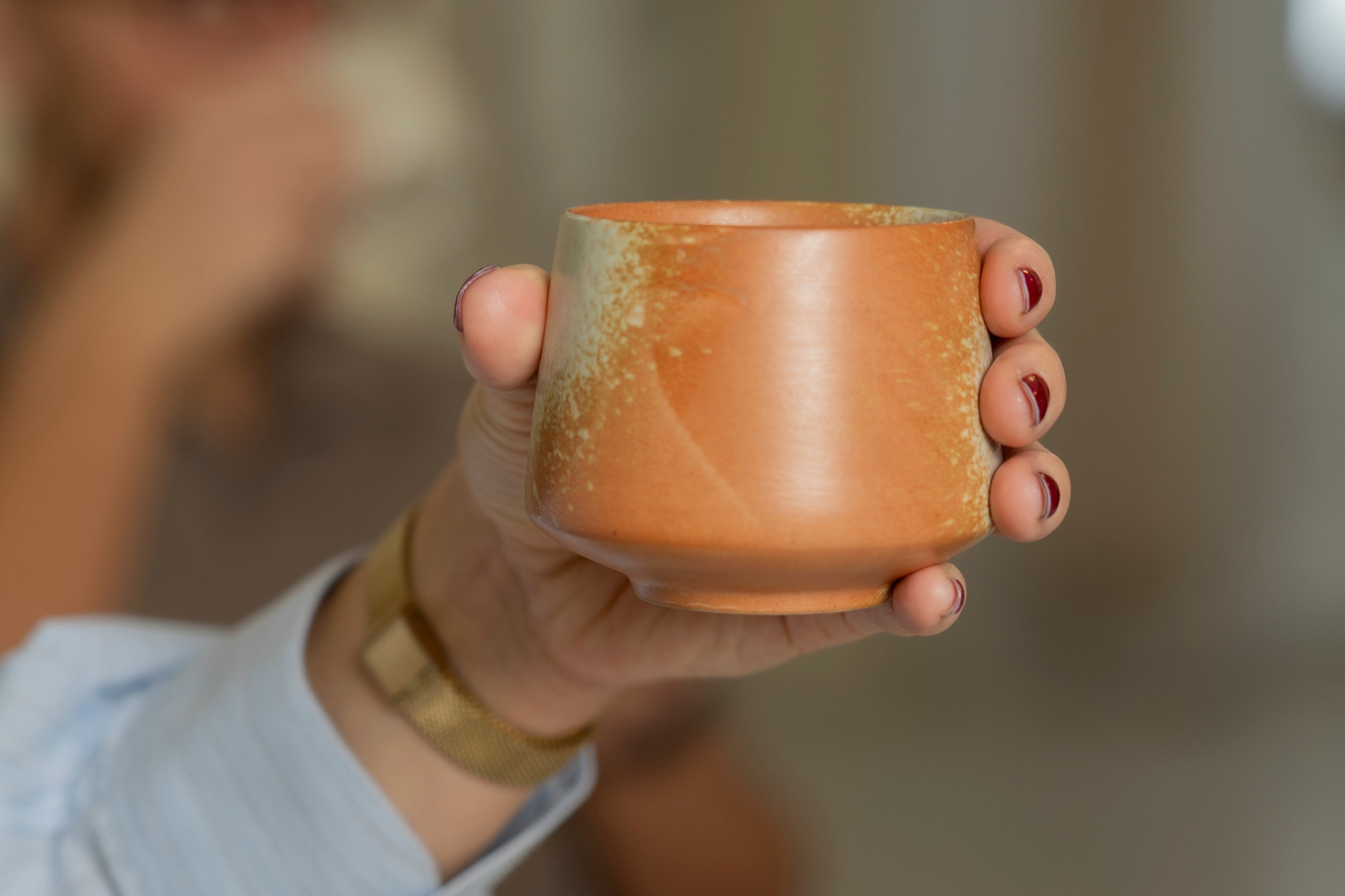 A hand holding our small ceramic cup 'Geisha' in the color rusty orange.