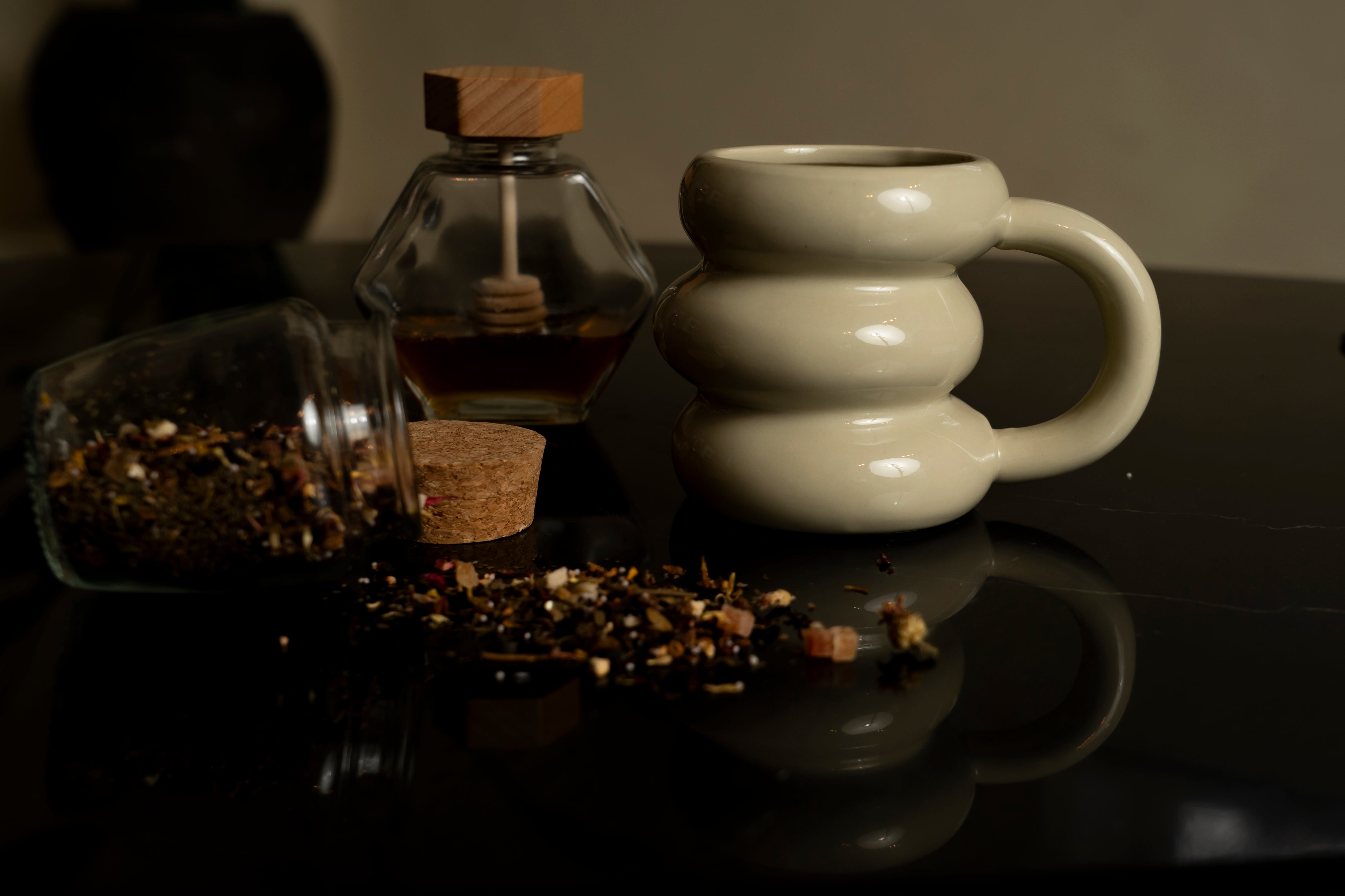 Our ceramic Donut mug in beige, next to a jar of fresh tea and some honey.