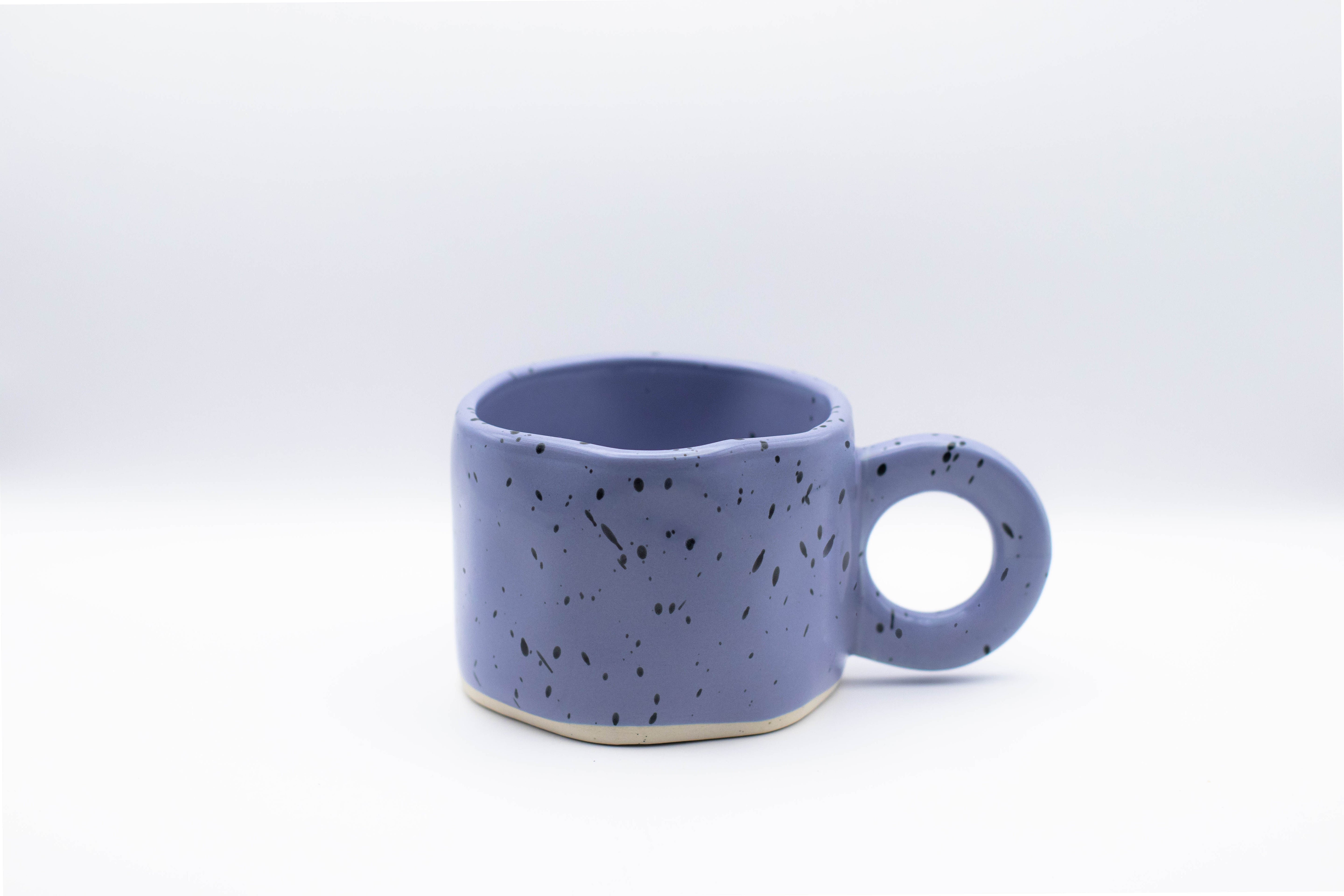 Stand-alone product picture of our purple ceramic cup Dotty with black paint splashes.