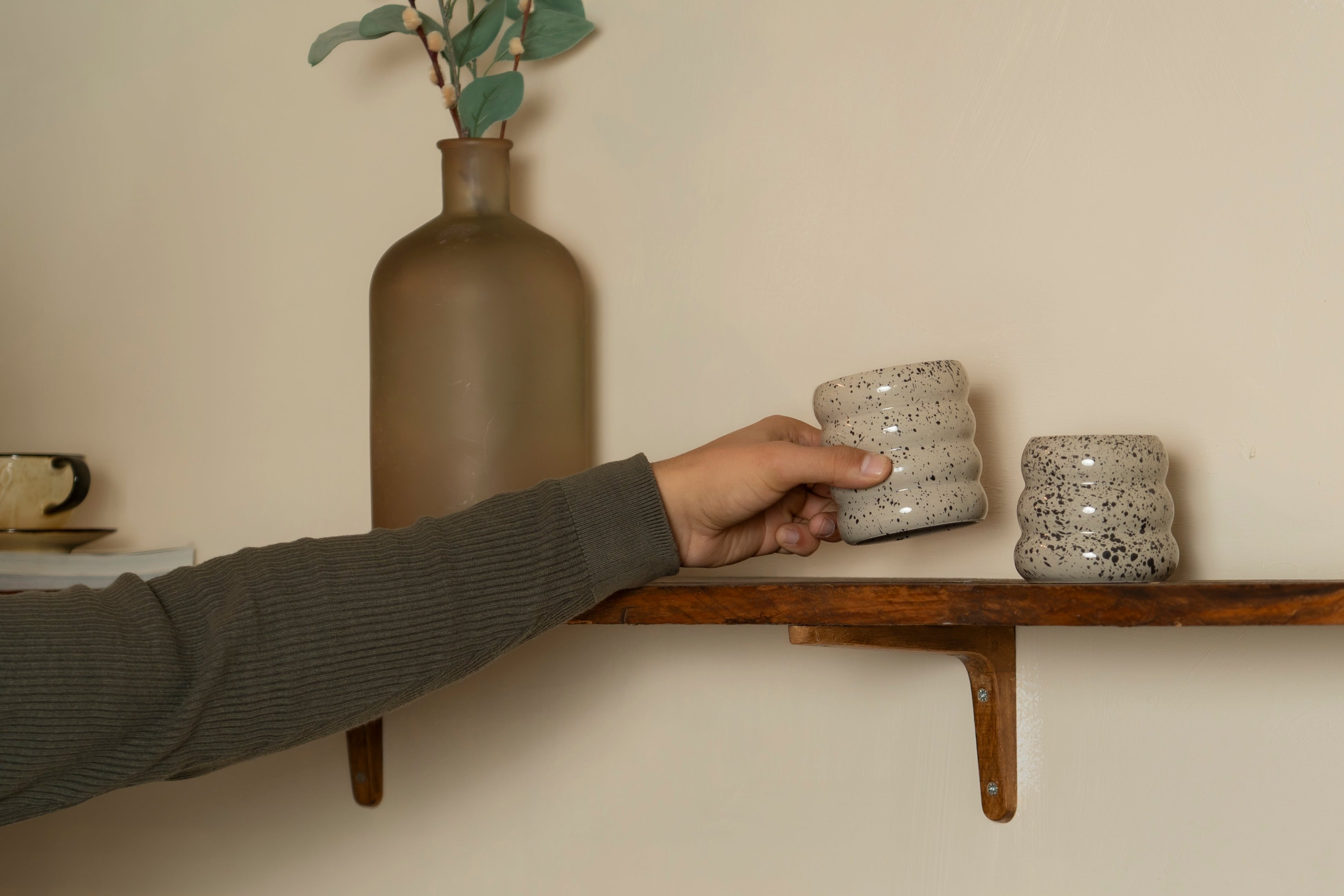 Someone grabbing our 4-layered ceramic mug "Sprinkled Donut" from a wooden shelf.