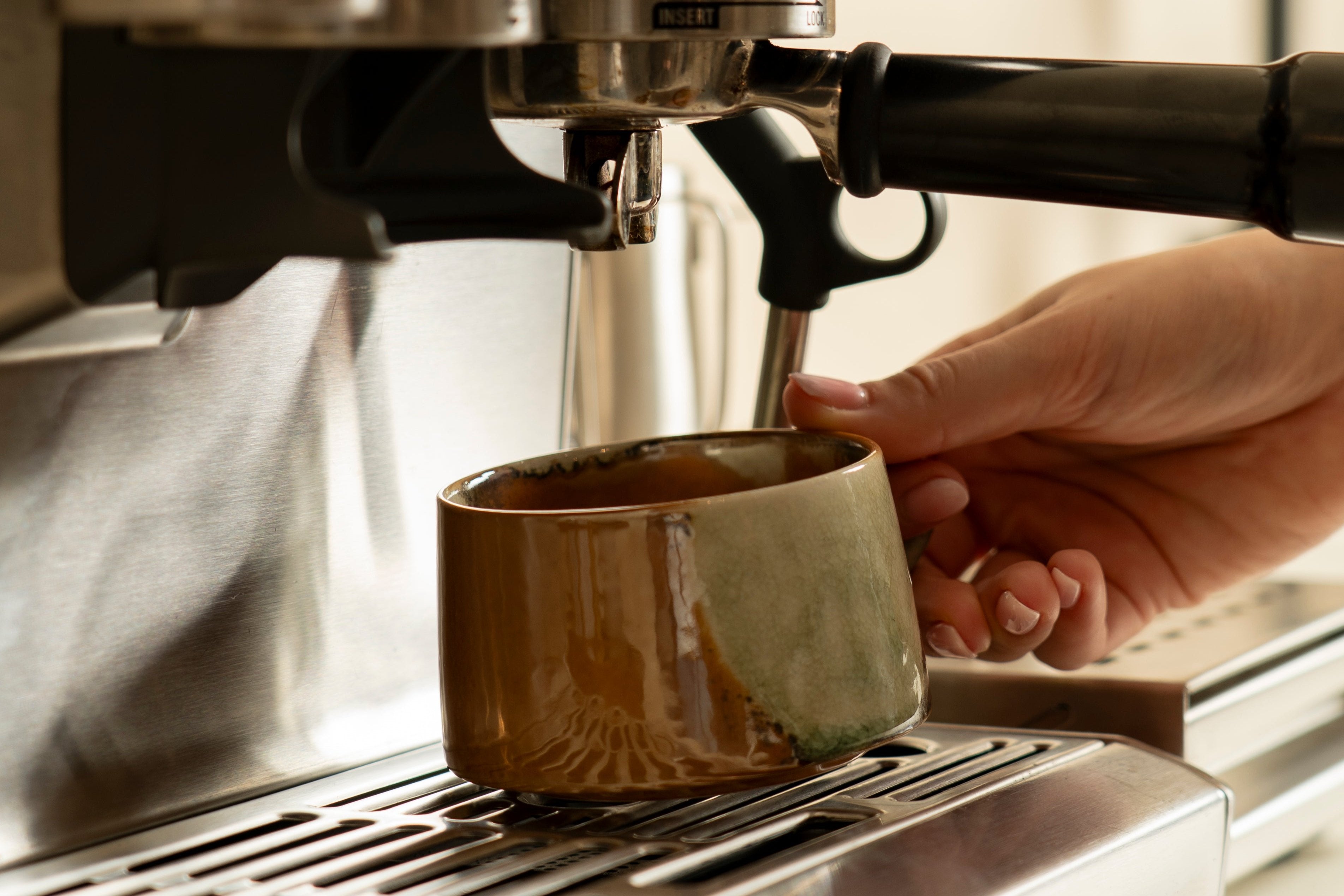 Picture of someone grabbing our Vintage Charm ceramic cup from underneath a coffee machine. 