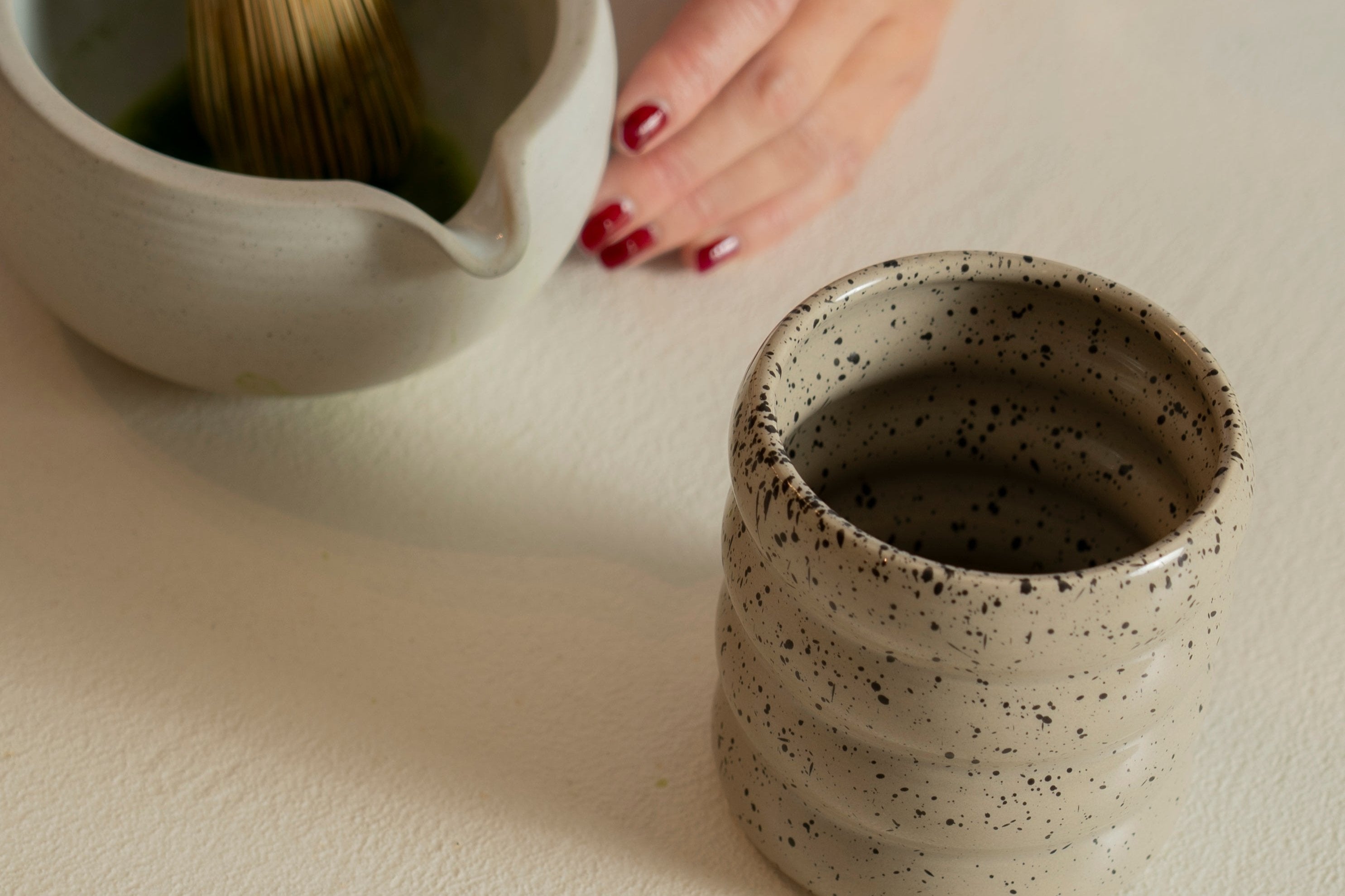 Picture of our 4-layered ceramic mug "Sprinkled Donut" while someone is making matcha on the background.