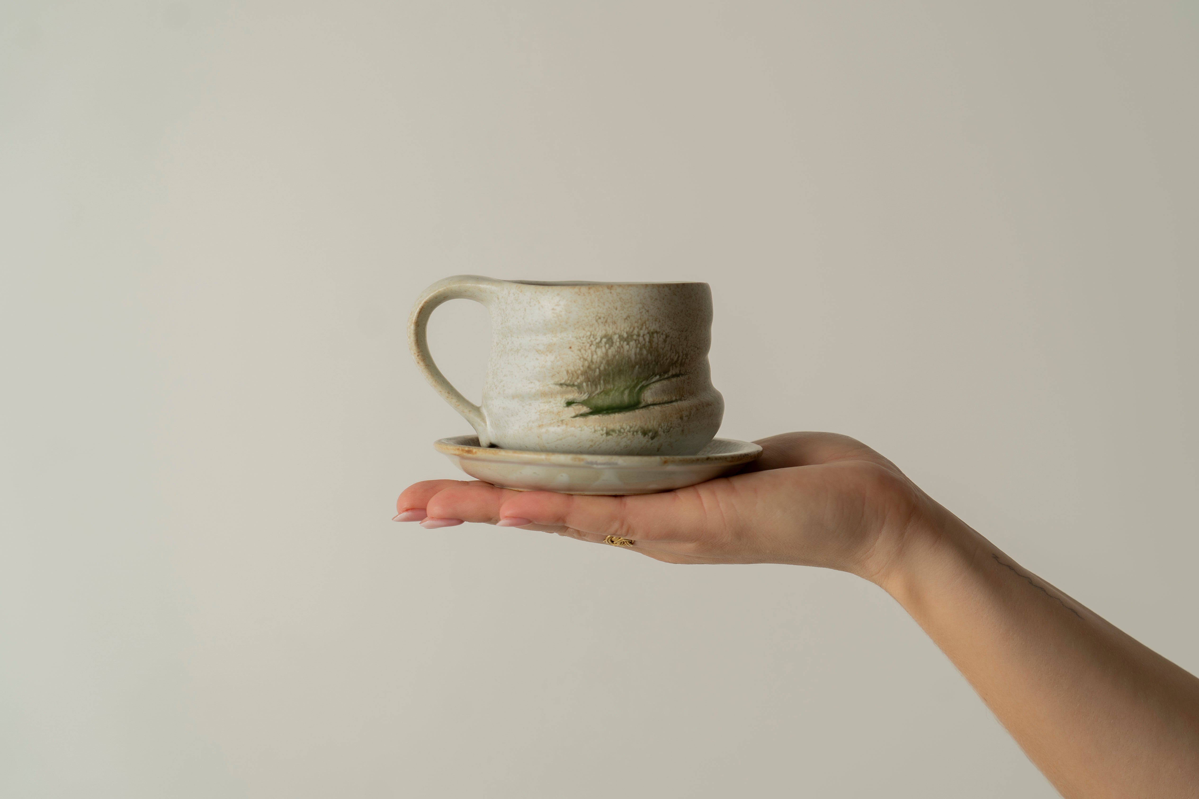 Picture of our ceramic cup Tsuyu on top of a hand, in a stone-grey color with bits of emerald green.