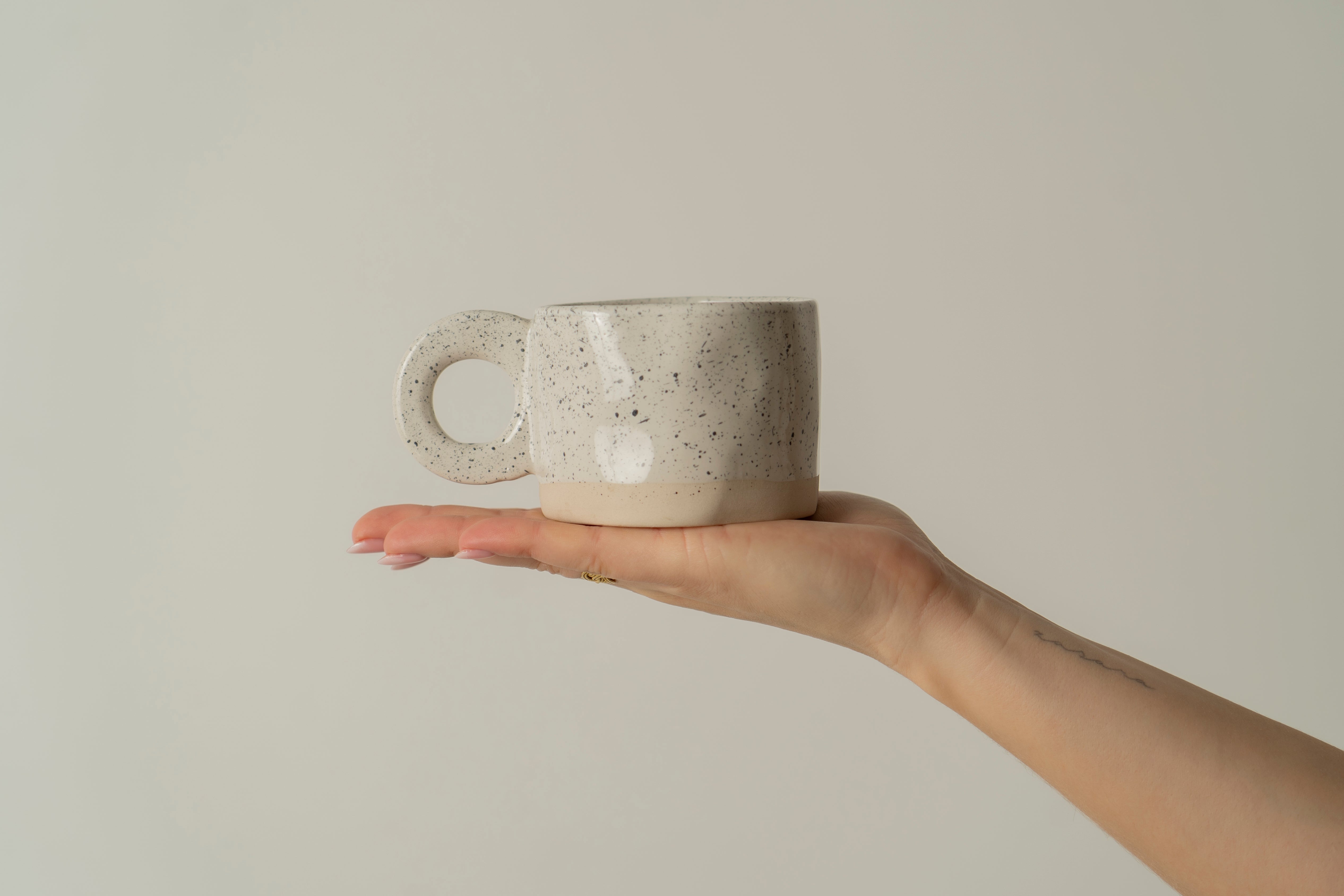 Picture of a hand holding our ceramic cup 'Dotty' in color white with black little dots.