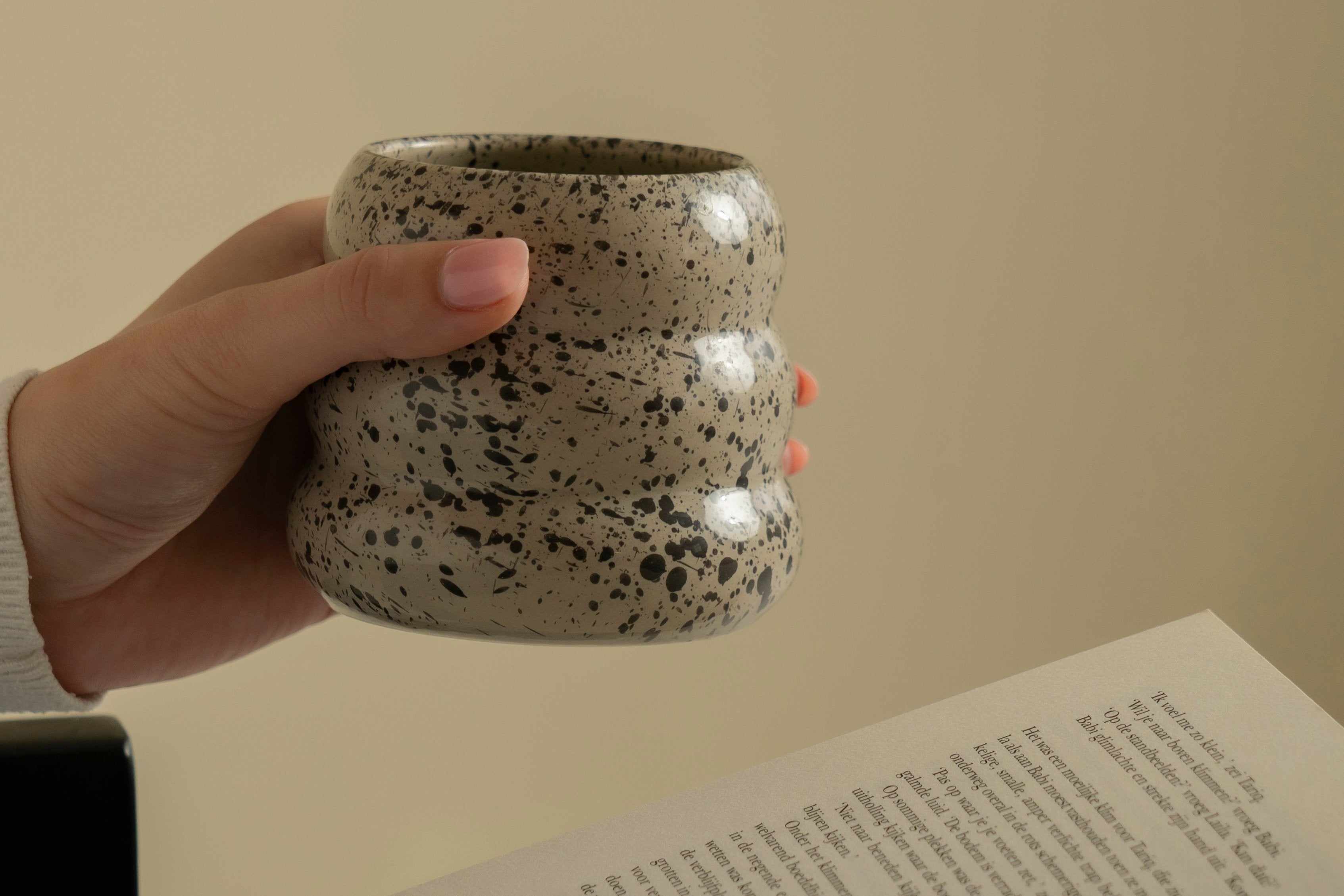 A hand holding our 3-layered ceramic mug "Sprinkled Donut" while reading a book.