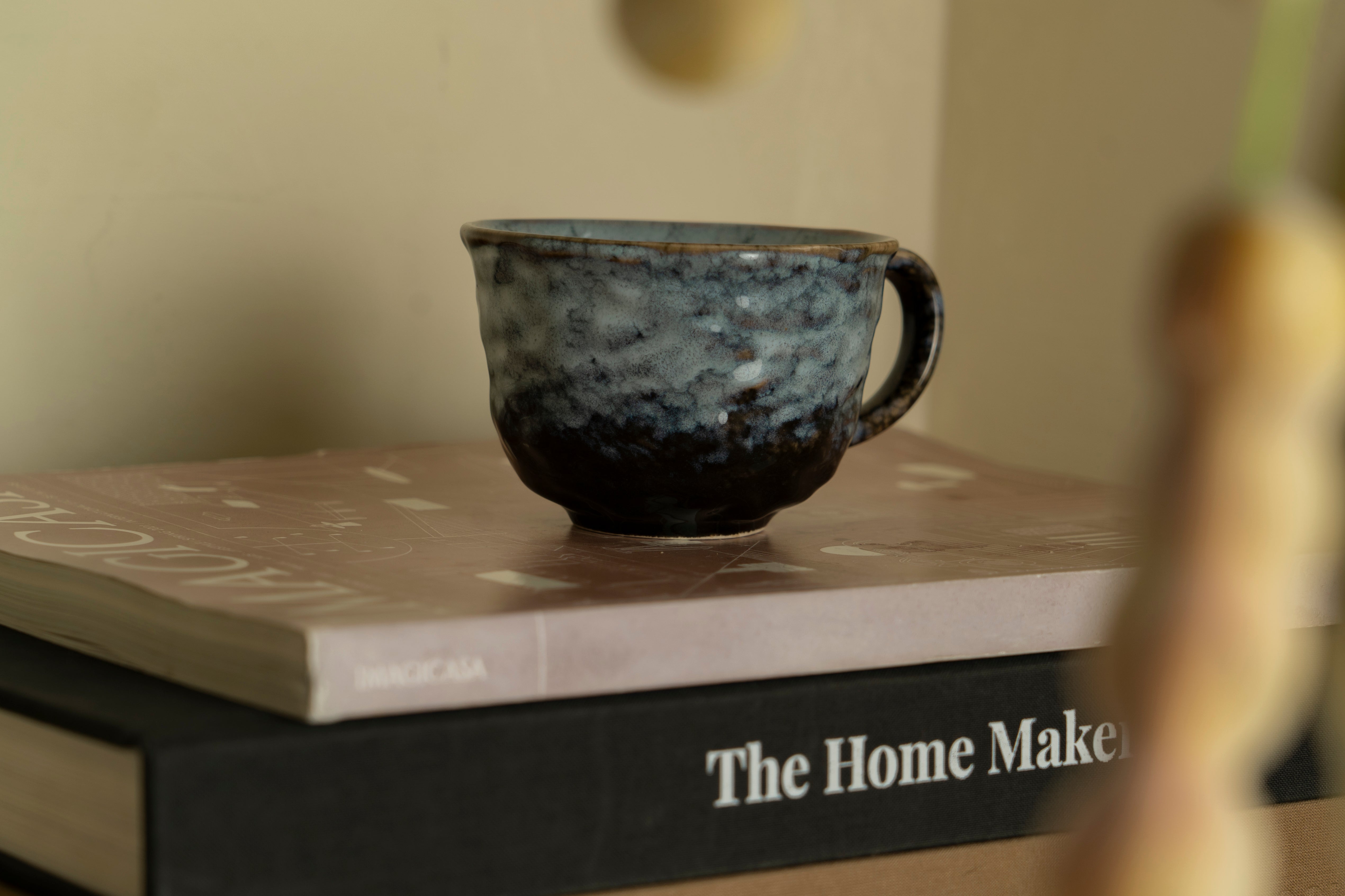 Aesthetic picture of our ceramic Sora cup with wobbly texture in a blue color, placed on top of two books.