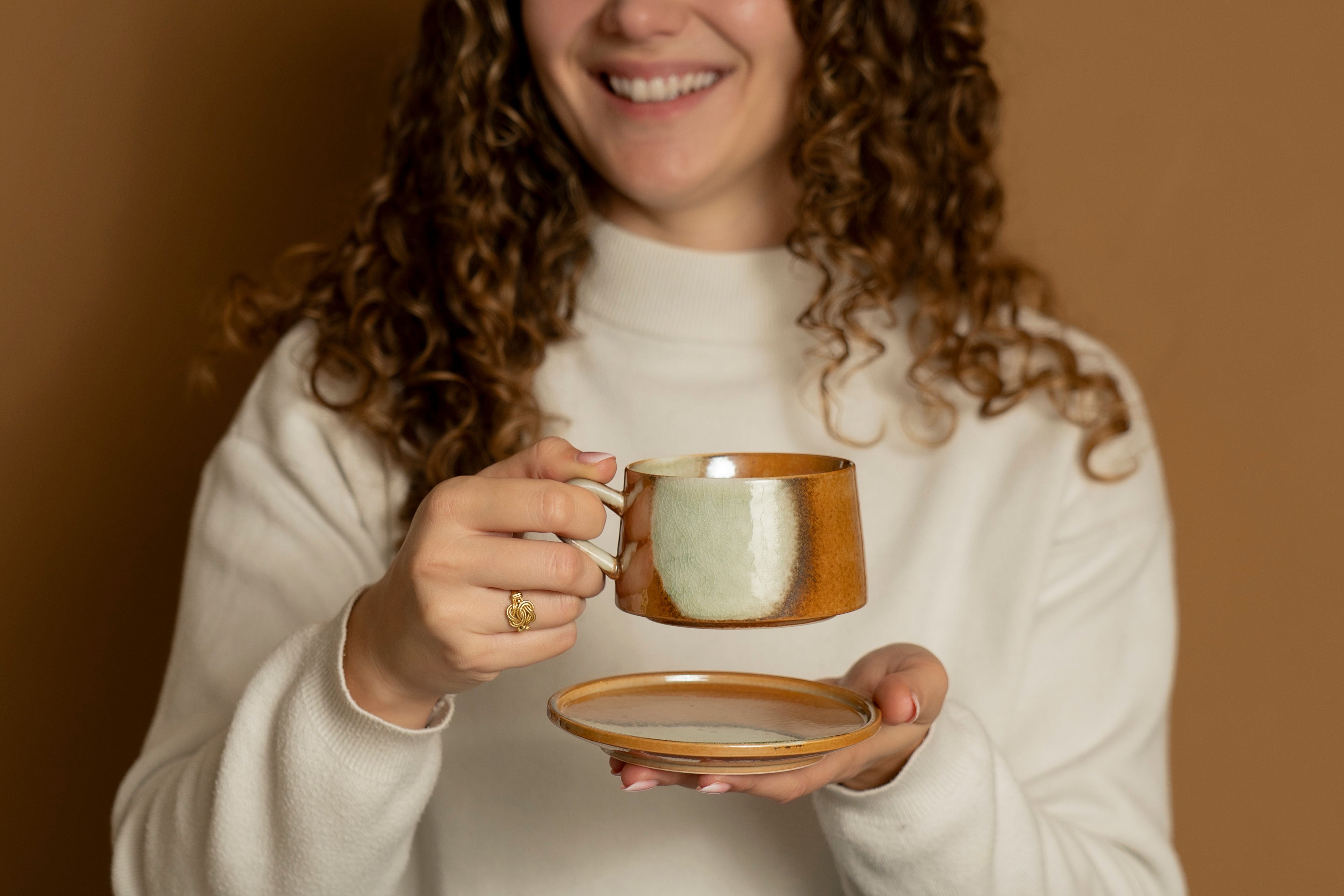 A picture of a woman holding our ceramic cup Vintage Charm, including saucer, in a deep orange marble tint.